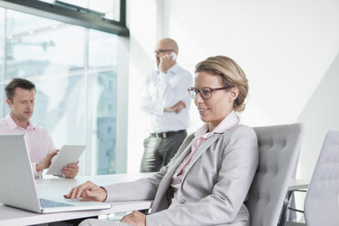 Three businesspeople with laptop, digital tablet and cell phone in conference room - RBF002156