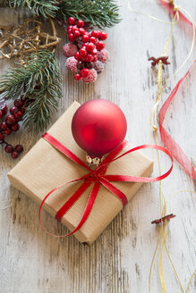 Eingepacktes Weihnachtsgeschenk mit roter Christbaumkugel auf Holz - SARF001149