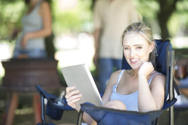 Smiling young woman sitting on a camping chair with a digital tablet - ZEF003283