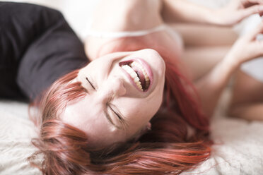 Young woman lying on bed laughing - ZEF002939