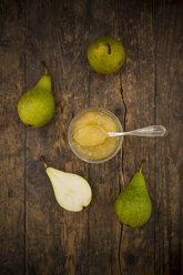 Whole and sliced organic pears and glass of pear jam on dark wood - LVF002474