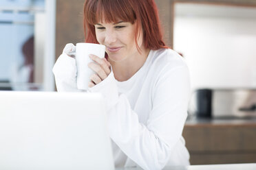 Young woman with laptop and cup of coffee in kitchen - ZEF002645