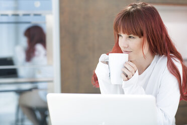 Young woman with laptop and cup of coffee in kitchen - ZEF002646