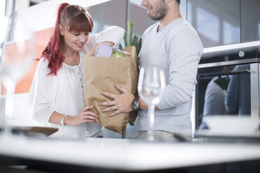 Couple in kitchen unpacking groceries - ZEF002665