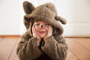 Porträt eines glücklichen kleinen Mädchens, das als Bär verkleidet auf einem Holzboden liegt - LVF002452