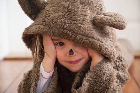 Porträt eines lächelnden kleinen Mädchens, das als Bär verkleidet auf einem Holzboden liegt, lizenzfreies Stockfoto
