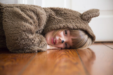 Porträt eines lächelnden kleinen Mädchens, das als Bär verkleidet auf einem Holzboden liegt - LVF002455