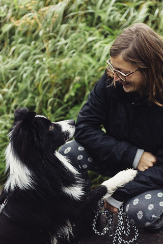 Lächelnde junge Frau im Gespräch mit ihrem Border Collie, lizenzfreies Stockfoto