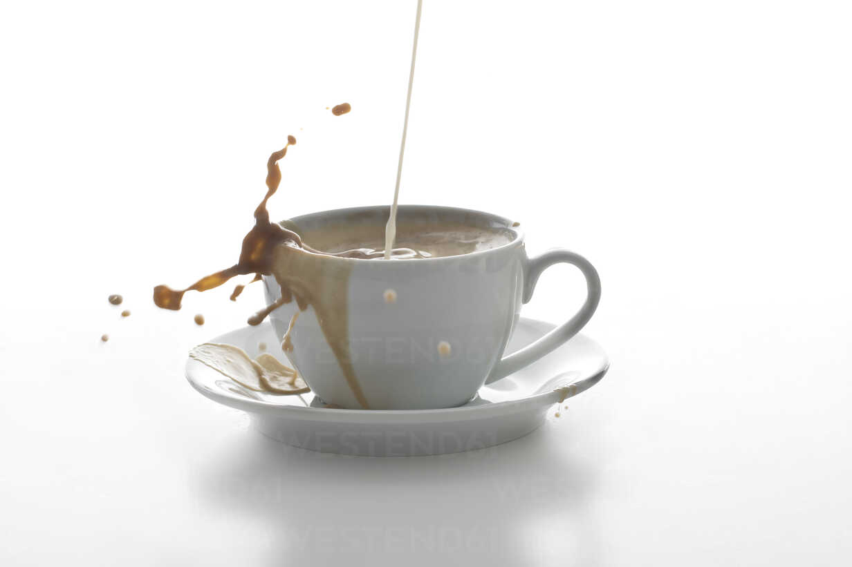 Milk splashing in a cup of coffee in front of white background
