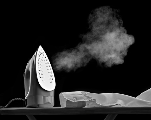 Dampfendes Bügeleisen und Hemdärmel vor schwarzem Hintergrund, lizenzfreies Stockfoto