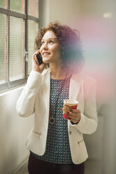 Junge Geschäftsfrau mit Handy und Blick aus dem Fenster - UUF002856