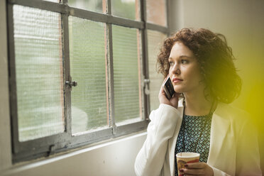 Young businesswoman on cell phone looking out of window - UUF002857