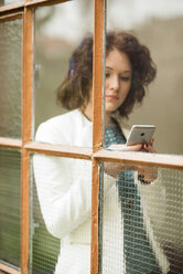 Junge Geschäftsfrau mit Mobiltelefon hinter dem Fenster - UUF002872