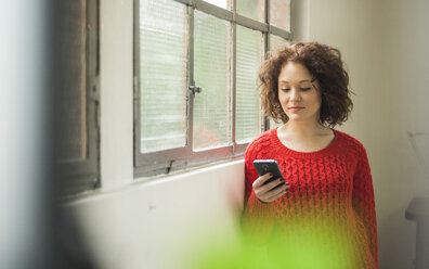 Junge Frau mit Mobiltelefon am Fenster - UUF002882