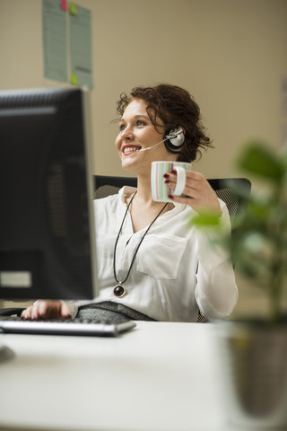 Smiling young woman in office wearing headset stock photo