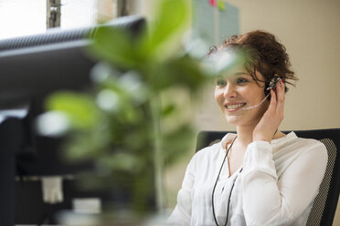 Lächelnde junge Frau im Büro mit Headset - UUF002914