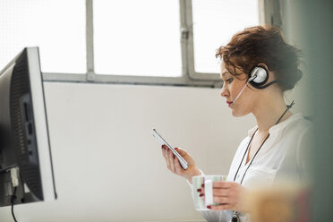 Young woman in office with headset and cell phone - UUF002915