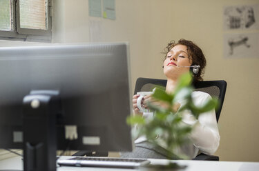 Junge Frau im Büro mit Headset lehnt sich zurück - UUF002918