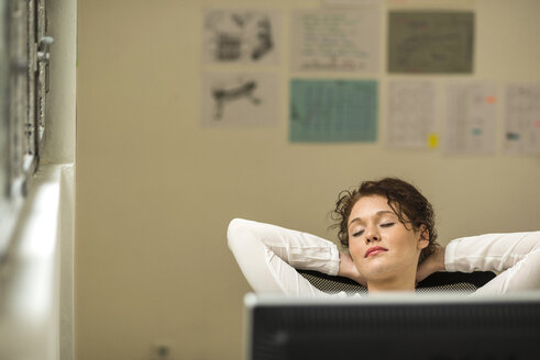 Young woman in office leaning back with eyes closed - UUF002920