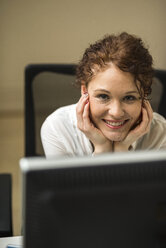 Porträt einer lächelnden jungen Frau am Schreibtisch - UUF002921
