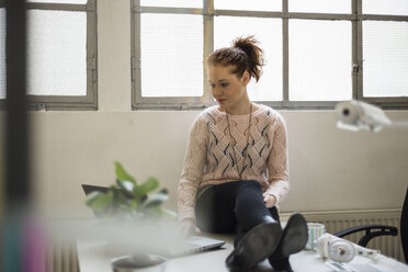 Young woman sitting on desk using laptop - UUF002937