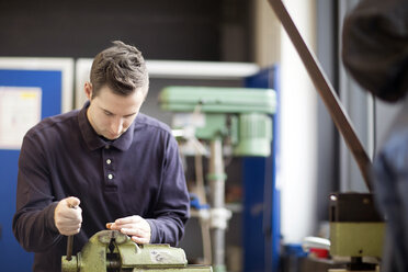 Young technician working at a bench vice in an industrial hall - SGF001235