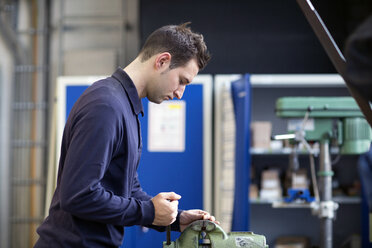 Young technician working at a bench vice in an industrial hall - SGF001236