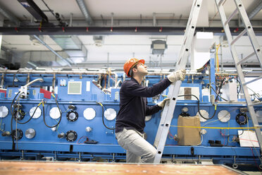 Young technician climbing up a ladder in an industrial hall - SGF001289