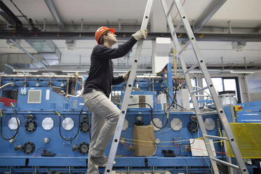 Junger Techniker steigt in einer Industriehalle auf eine Leiter - SGF001290