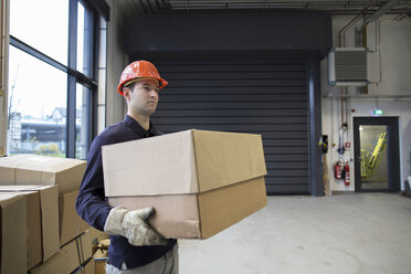 Young technician carrying cardboard box at an industrial hall - SGF001239