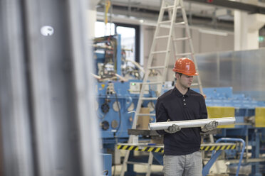 Junger Techniker trägt Rohre in einer Industriehalle - SGF001240