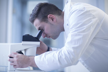 Scientist in lab looking through light microscope - SGF001248