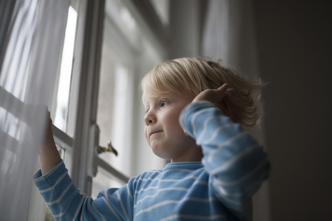 Kleiner Junge schaut aus dem Fenster und wartet, lizenzfreies Stockfoto