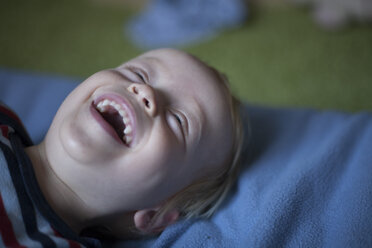 Porträt eines lachenden kleinen Jungen auf dem Bett liegend - RB002199