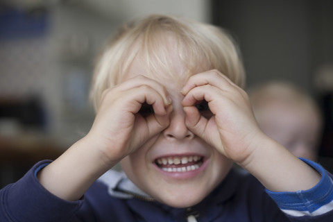 Porträt eines lächelnden kleinen Jungen, der durch seine wie eine Brille geformten Hände schaut, lizenzfreies Stockfoto