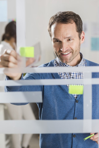 Geschäftsmann mit Haftnotizen an Glasscheibe, lizenzfreies Stockfoto