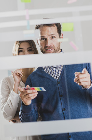 Geschäftsmann und Geschäftsfrau mit Haftnotizen an Glasscheibe, lizenzfreies Stockfoto