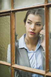 Young businesswoman on cell phone looking out of window - UUF002999