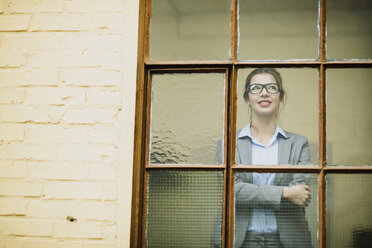 Lächelnde junge Geschäftsfrau schaut aus dem Fenster - UUF003003