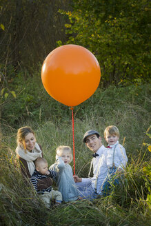 Family sitting with balloon on meadow - JTLF000014