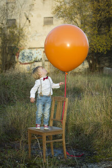 Junge auf Stuhl stehend mit Luftballon auf Wiese - JTLF000009