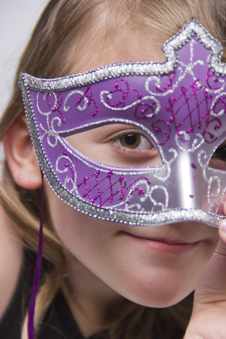 Mädchen hält sich Karnevalsmaske vor das Gesicht, lizenzfreies Stockfoto