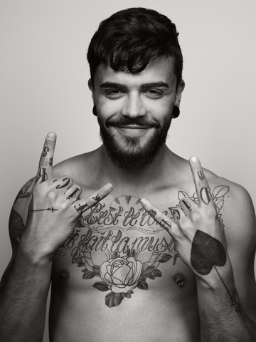 Porträt eines grinsenden Mannes mit Tätowierung auf Brust und Händen, lizenzfreies Stockfoto
