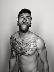 Portrait of man with tatoo on his chest sticking out tongue - STK001123