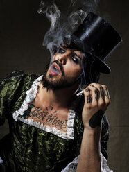 Porträt eines rauchenden Mannes mit Vollbart und Augen-Make-up, der einen Zylinderhut und ein barockes Kleid trägt - STK001126