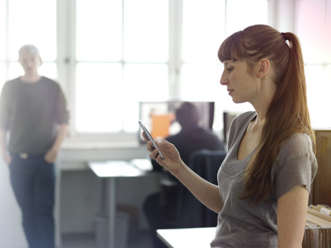 Frau im Büro schaut auf ihr Handy, lizenzfreies Stockfoto