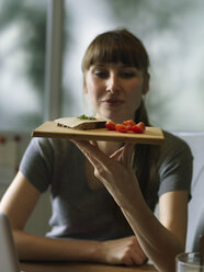 Frau am Schreibtisch hält Tafel mit Snack - STKF001171