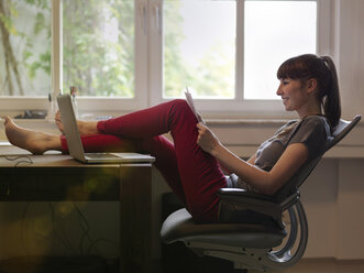 Frau mit Füßen auf dem Schreibtisch beim Lesen von Papier - STKF001190