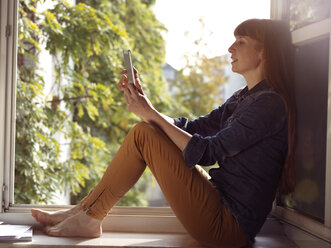 Frau am offenen Fenster mit Handy in der Hand - STKF001162