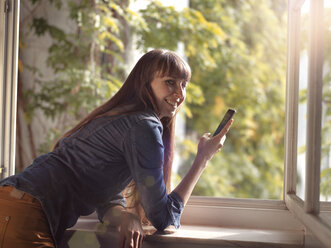 Smiling woman at open window holding cell phone - STKF001160